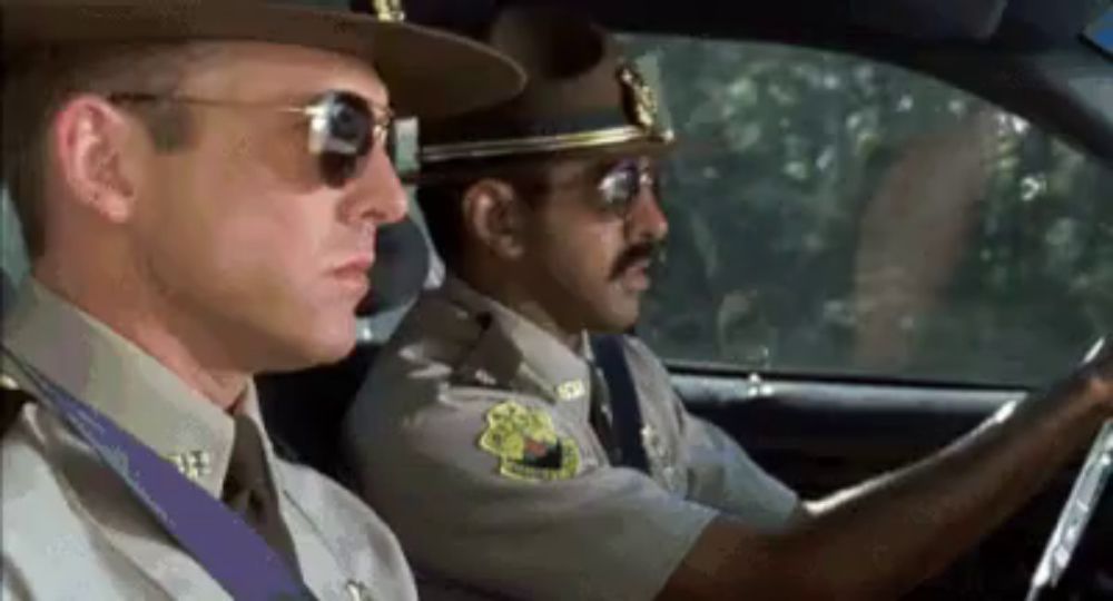 two police officers are sitting in a car wearing sunglasses .