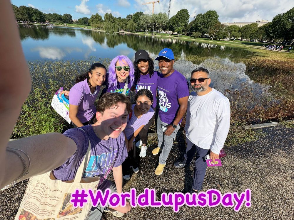 A group of doctors, nurses, and students wearing purple clothes and wigs smiles in a group photo. 