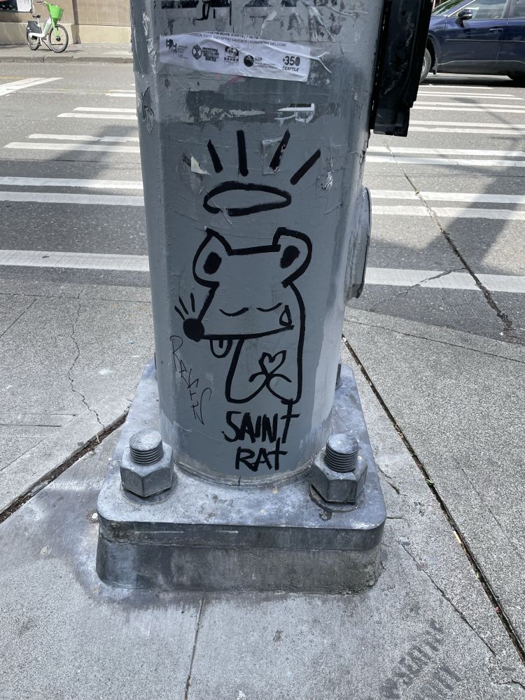 Graffiti of a crying rat holding a heart with a halo. Below them is written “saint rat”