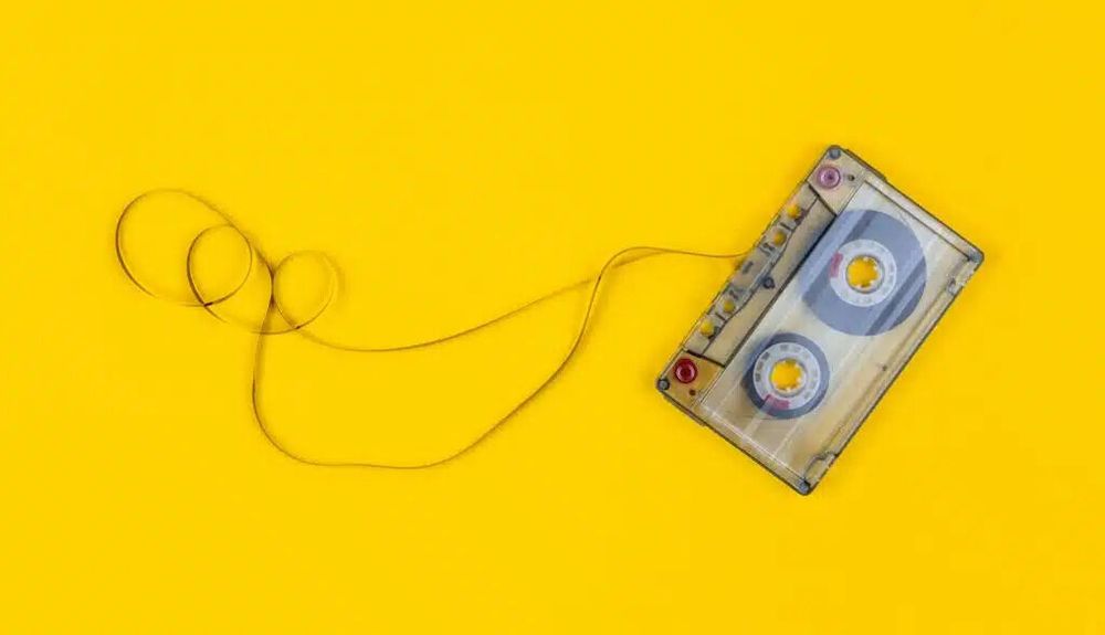 A cassette tape, unwound with the tape out, against a yellow background.