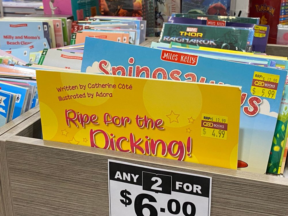 A tray of children’s books in tub at a bookstore, standing up. The bin covers the bottom half of the books, resulting in the front book appearing to be titled “Ripe for the Dicking!”