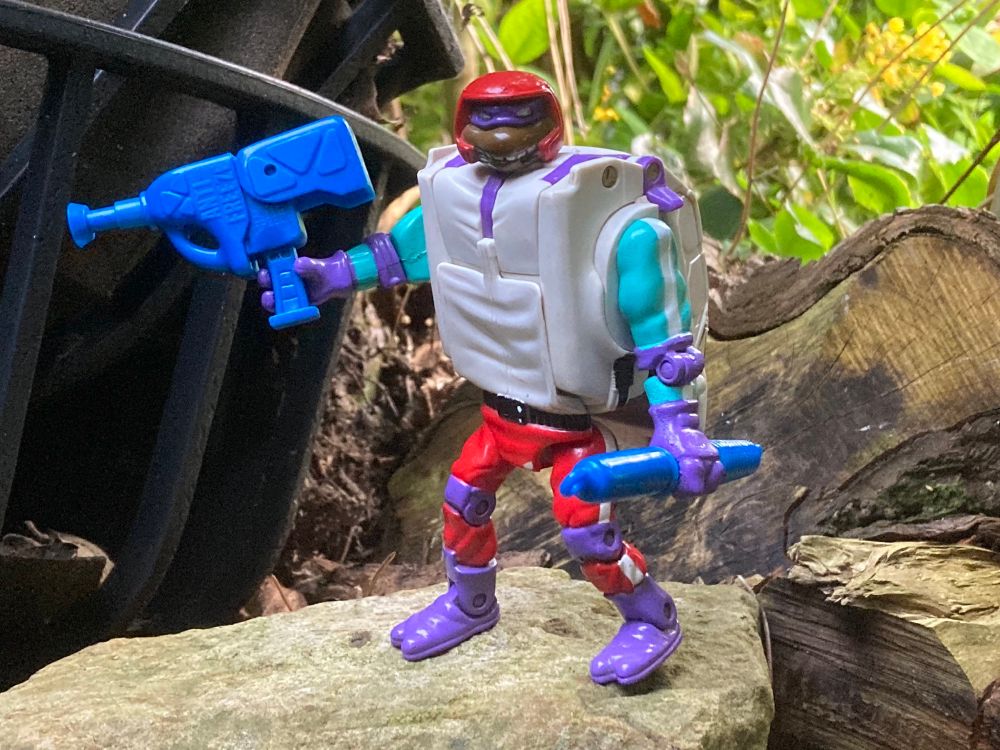 Teenage Mutant Ninja Turtles Road Ready Mutations Don - a Donatello clad in a very early 90s racing driver outfit holding a large blue blaster and spring weapon