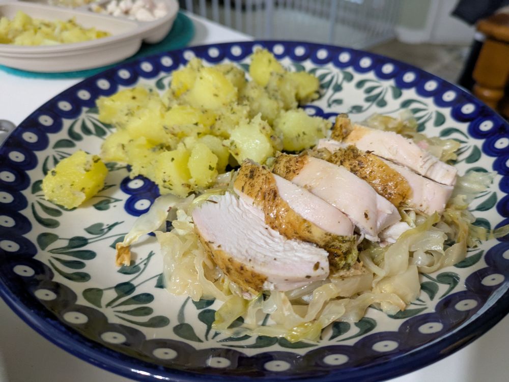 A plate with chicken breast served atop cooked cabbage with a side of potatoes with herbs