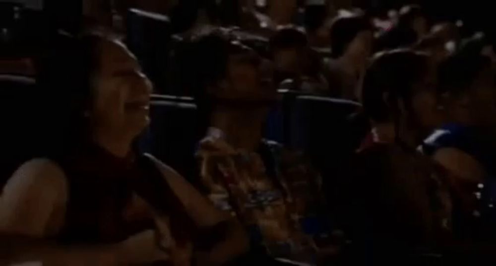 a man is sitting in a theater watching a movie while holding a can of soda .