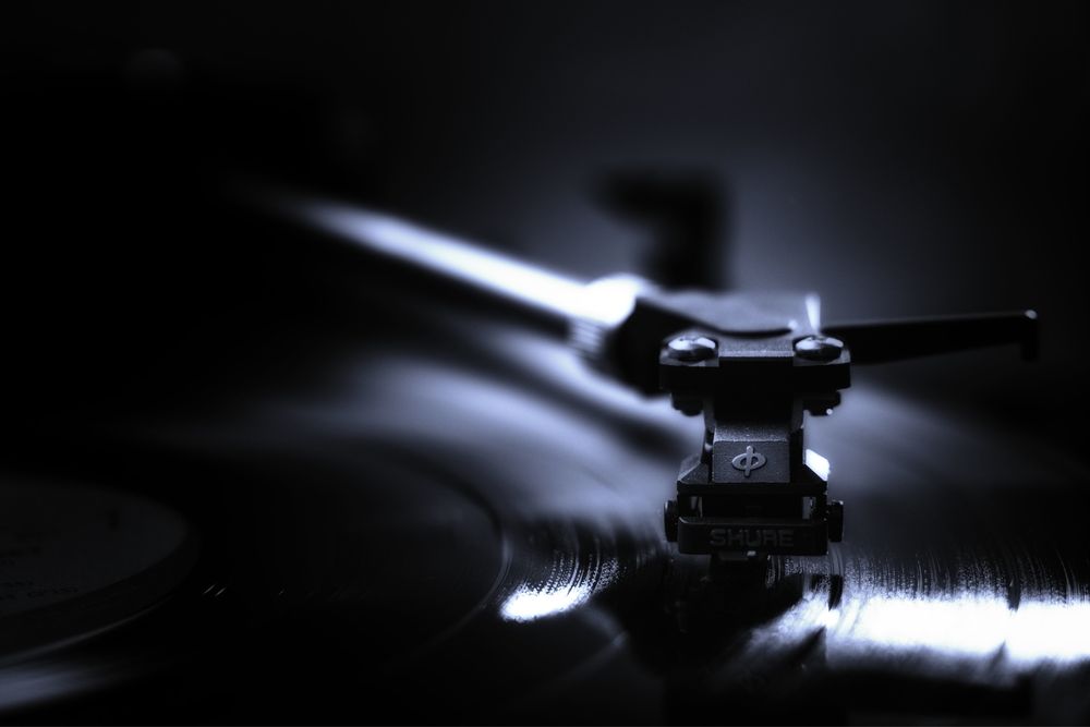 A close-up of a record player's needle captures the glossy grooves of a vinyl record in low lighting. The image emphasizes the intricate details and reflections of a vintage turntable. Record players are making a huge comeback for the music afficionados.