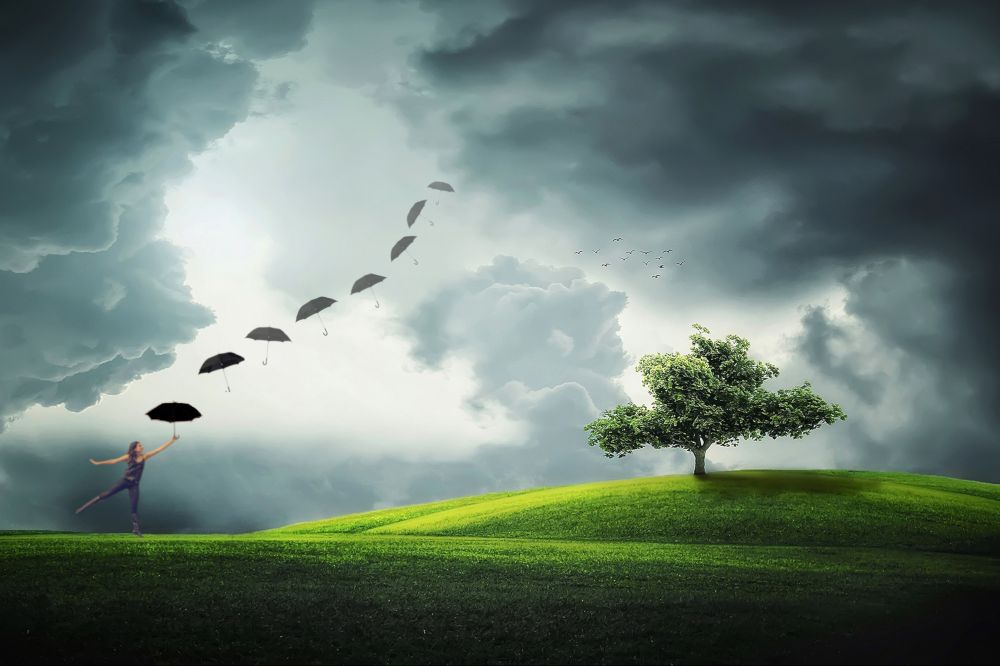 A whimsical image of a girl dancing on a grassy hill, holding an umbrella in the wind, while a series of umbrellas float upwards. Dark, dramatic clouds loom in the sky, and a lone tree stands on the hill.