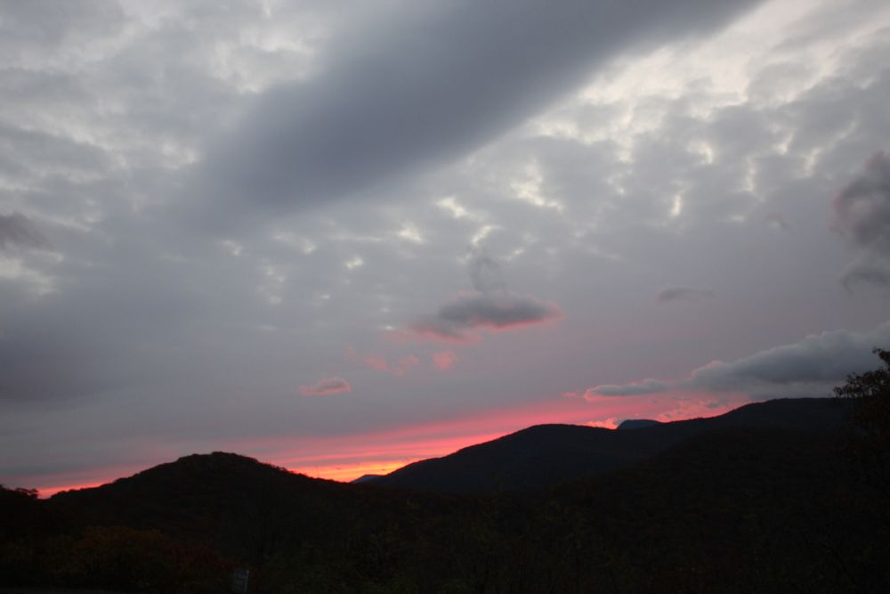 Orange and pink glow along a mountain ridge beneath gray clouds