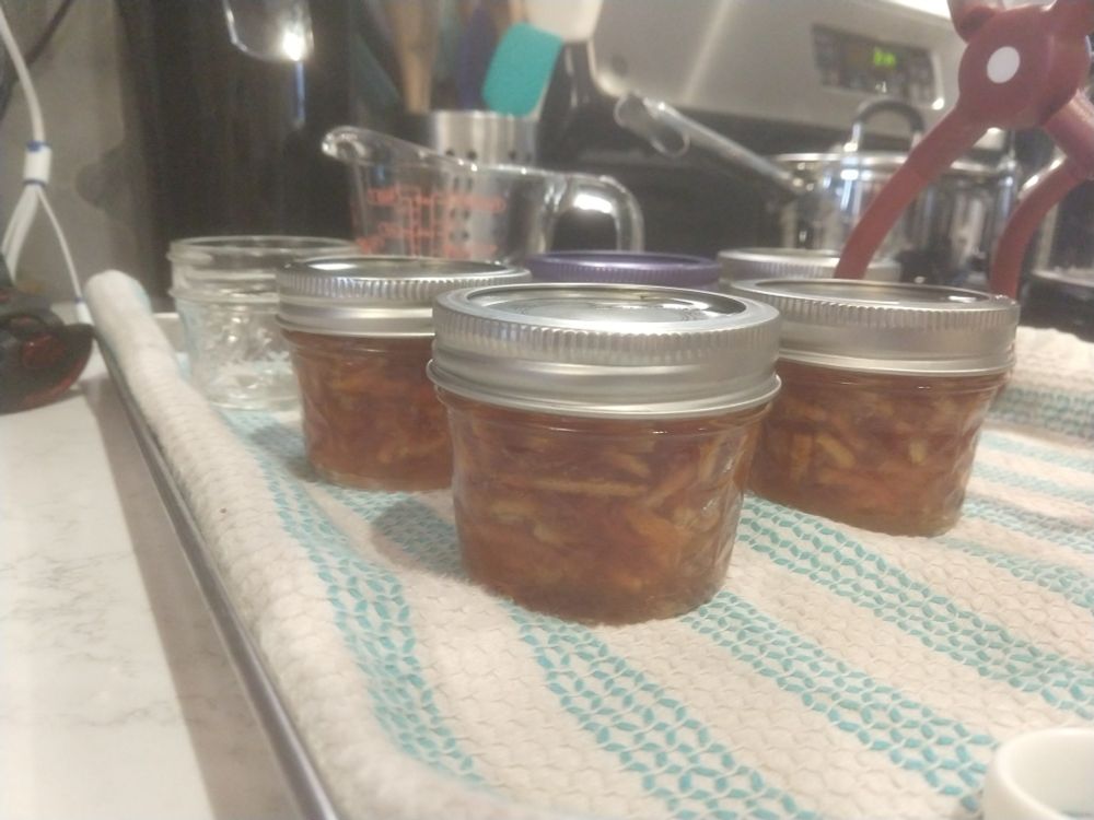 Three glass jars of homemade marmalade sitting on a blue and white striped dish towel
