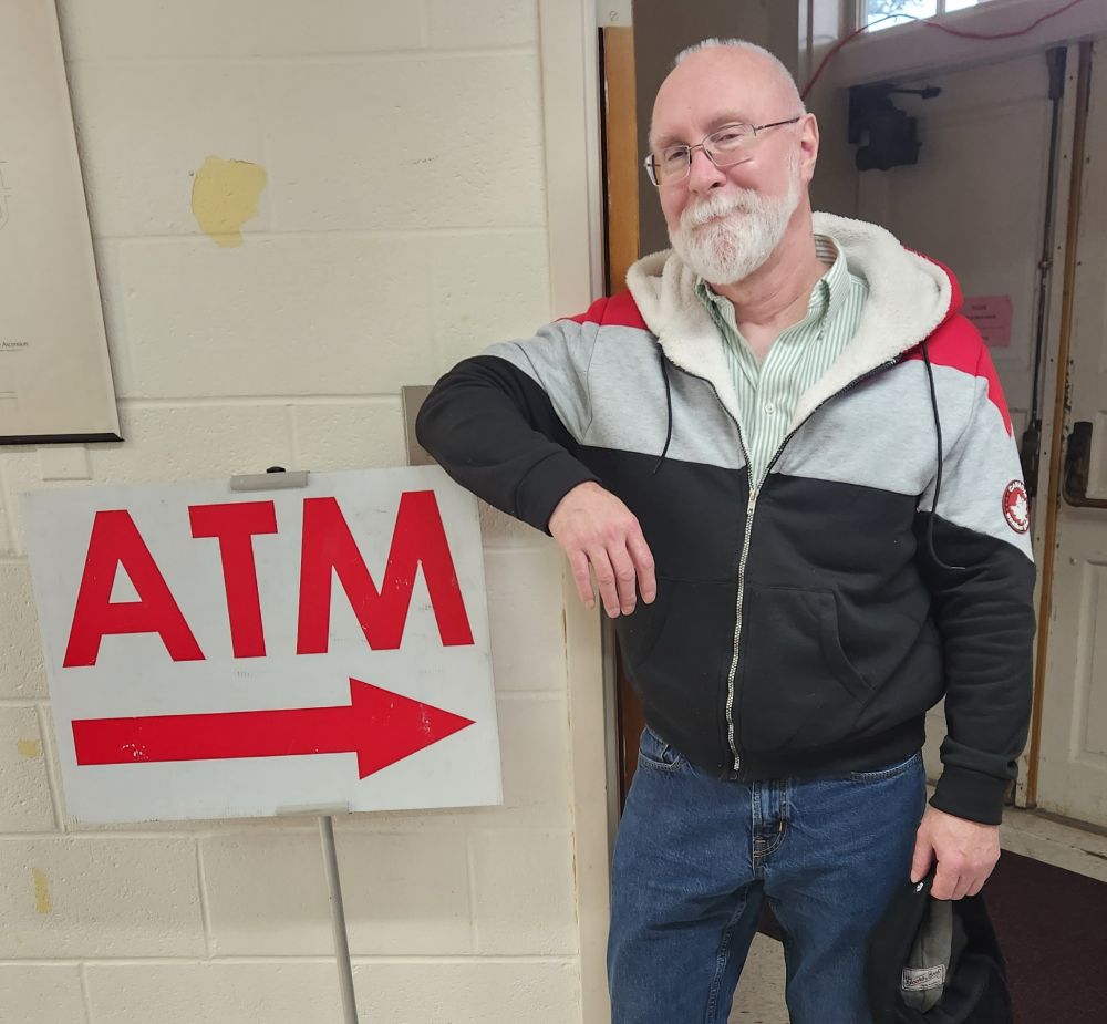 Old guy leaning on a sigh which reads "ATM", pointing to him.