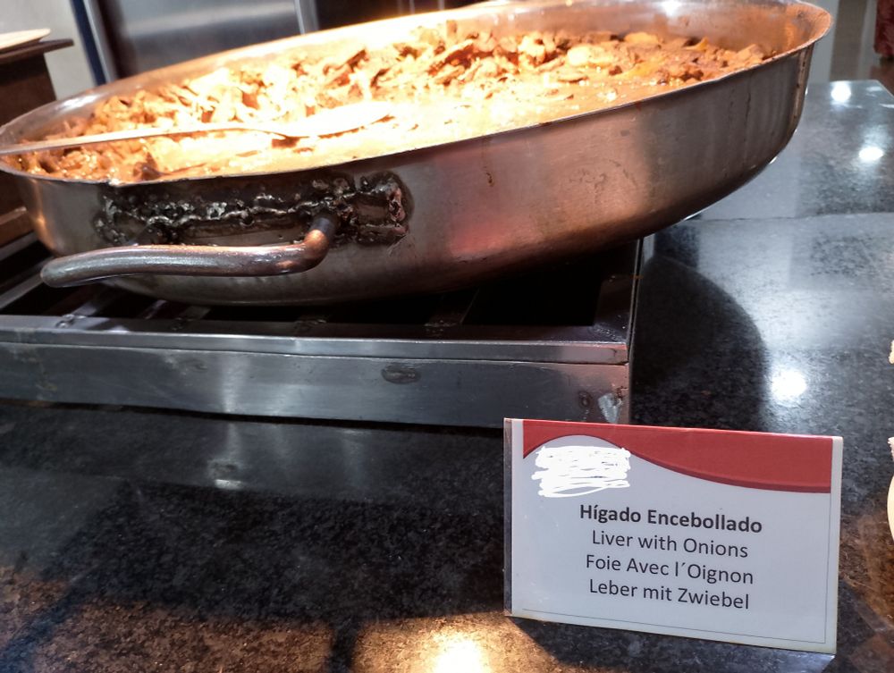picture of liver and onions in a big ol pan. theres a sign next to it that says "Liver with Onions" in various languages