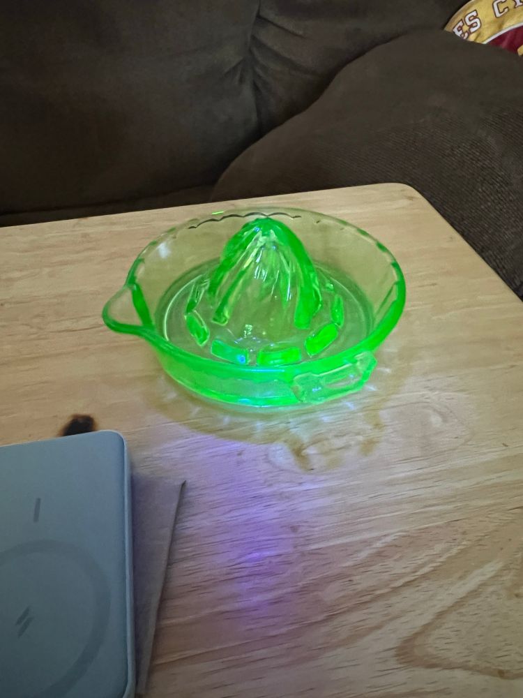 An antique green glass citrus juicer, glowing bright green under a UV flashlight. 