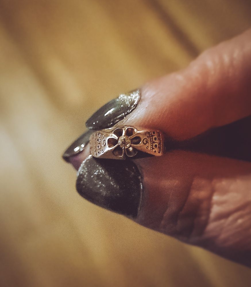 Fingertips holding a delicate, engraved gold ring with one tiny diamond in a buttercup setting.