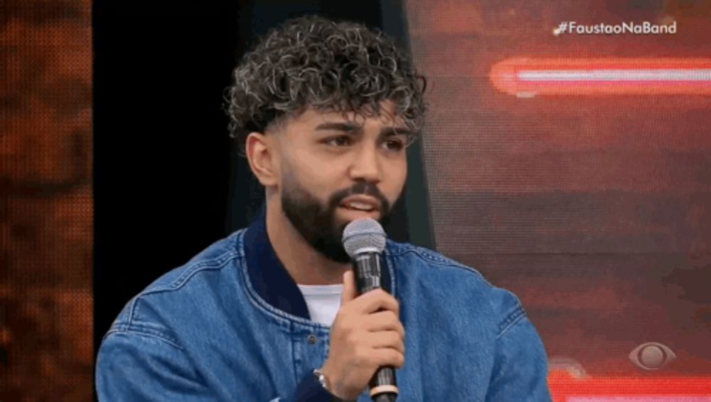 a man with a beard is holding a microphone in front of a screen that says faustao no band