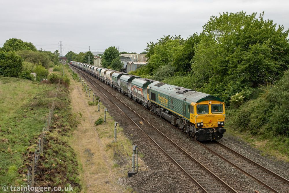 a green & yellow railway locomotive is hauling some green or grey wagons through a leafy scene