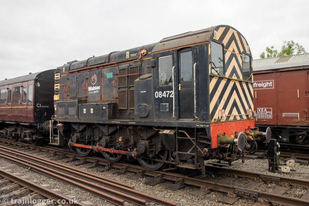 a small black locomotive with yellow and black "wasp stripes" on the end is seen parked in a siding