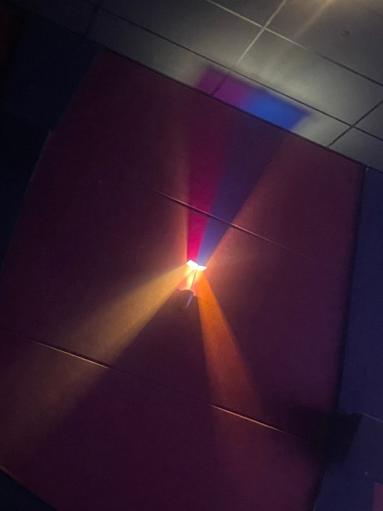 photo of movie theatre light with pink and blue filters shining a bisexual flag on the wall and ceiling 