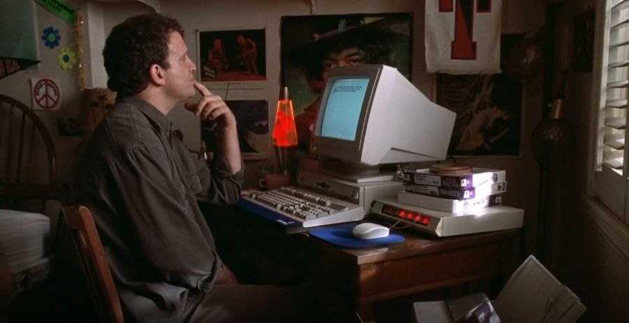 Image extrait du film Mother d'Albert Brooks dans lequel l'acteur et réalisateur joue un romancier. Sur l'image, il est dans sa chambre d'enfant chez sa mère (posters de Hendrix, poster Peace & Love, etc.) : on le voit pensif, sur le doigt sur la bouche, assis face à une page de traitement de texte d'un ordinateur dernier cri... mais dernier cri pour 1996.