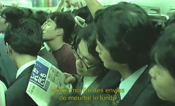 Screencap de "Angel Dust" de Sogo Ishii. 
Deux salarymen discutent dans le métro bondé. L'un a un journal dans les mains et dit à son collègue en se penchant vers lui pour être un peu discret une phrase que le sous-titre ici incrusté nous traduit : "Même moi j'ai des envies de meurtres le lundi".