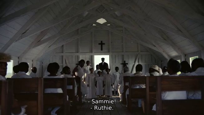 Screenshot of the film, showing a Black congregation in a small white wooden church, all dressed in white except the preacher at the front in black.

Caption reads: "Sammie!  Ruthie."
