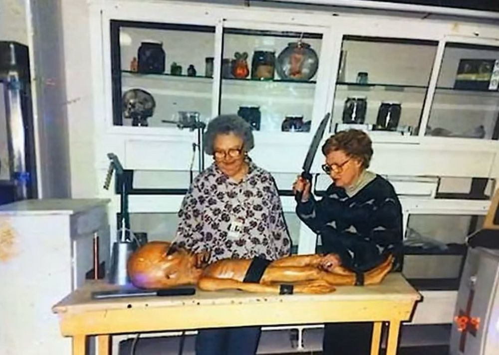 Two old ladies observe a grey style alien strapped to a table. One lady wields a knife as though she’s about to give this guy a chop. 
