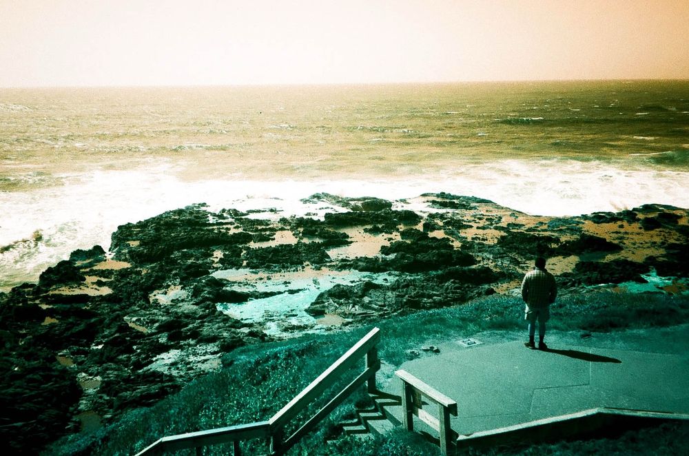 A man looks out at the ocean. taken with Lomo Turquoise film which makes the sky orange and earth tones turquoise.
