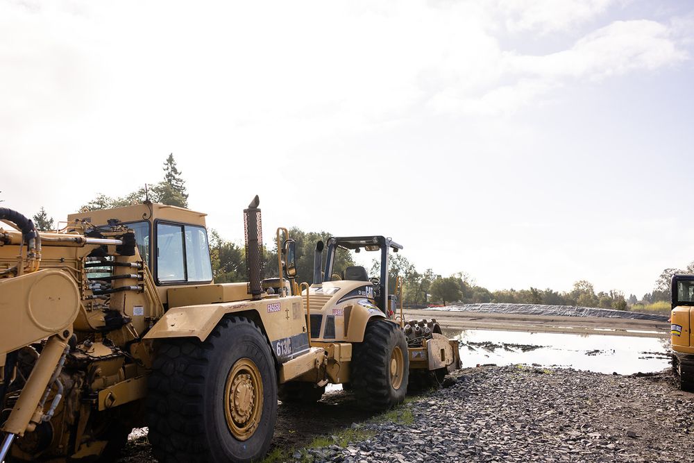 in the foreground there is a tractor and other construction equipment on a muddy field with a blue sky in the background 