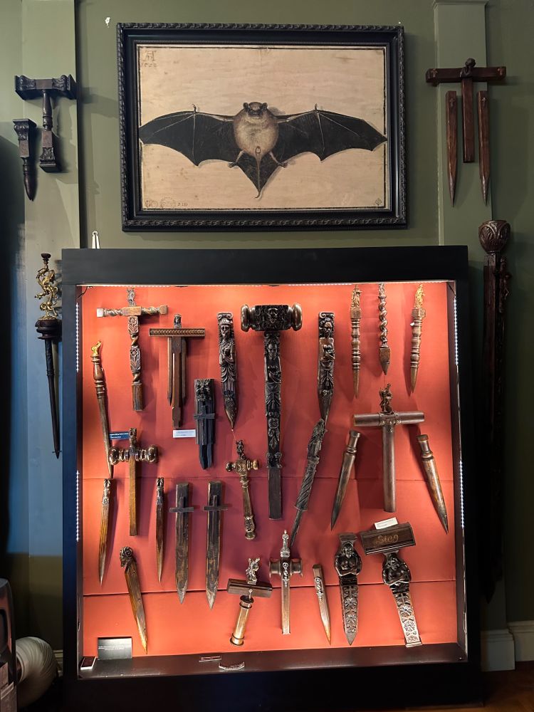 an assortment of wooden crucifixes, mallets, and spikes in a display case, below an image (maybe an etching) of what my niece said is 