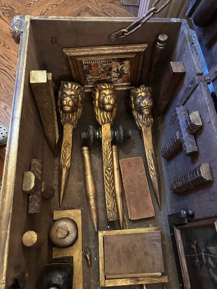 This is a photo of an antique wooden trunk, likely from the 1860s, full of various implements for killing vampires, including golden stakes with carved lions' heads, religious iconography, holy water, and a bible.