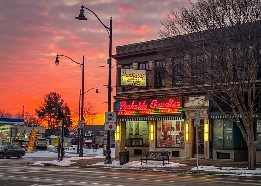 The exterior of Parkside Candy lit up in neon along with a vibrant sunset.