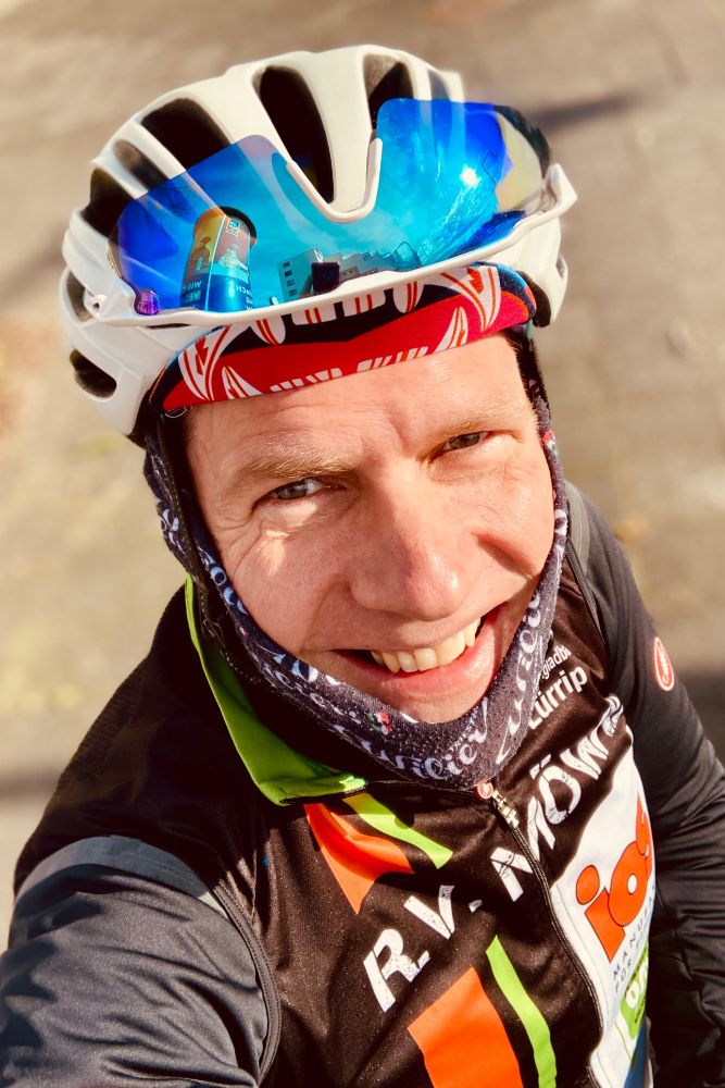 Selfie von mir in Rennradklamotten mit Helm, Sonnenbrille auf den Helm gesteckt, Winterjacke und Vereins-Wind-Weste.