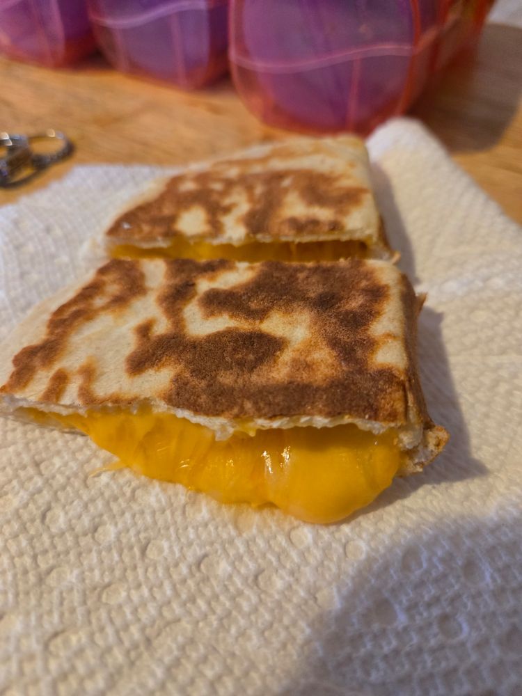 Half of a cheese tortilla all oozy and melty sitting on a paper towel. Its not like a quesadilla because this type is rolled out then stuffed with cheese, only then does it go onto the comal to cook the tortilla and melt the cheese. A pueblo native treat! (My husband is from Jemez Pueblo NM)