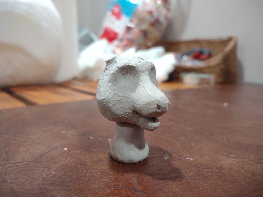 A small clay sculpture of a cartoonish goat head without horns or much detail (side view)