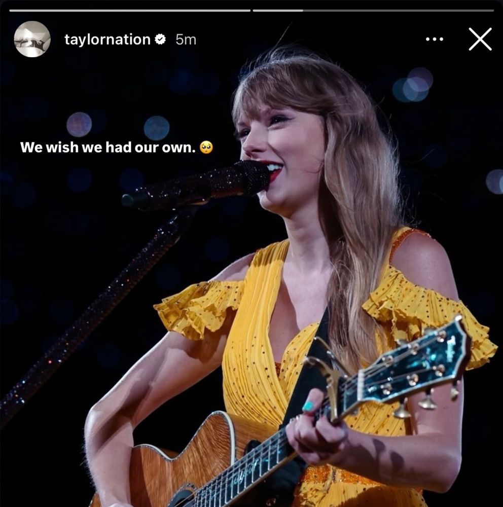 A picture of Taylor Swift performing at The Eras Tour during the Acoustic Section. In the photo, Taylor is holding a guitar and wearing a yellow dress.