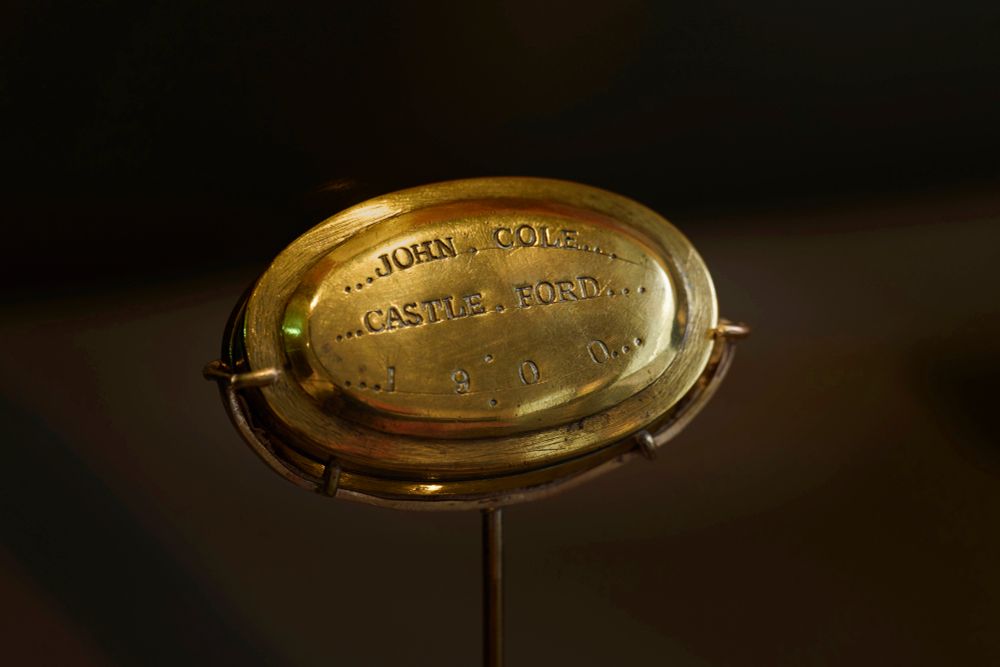 A brass oval box. Text roughly punched into the lid reads: John Cole, Castle Ford, 1900'