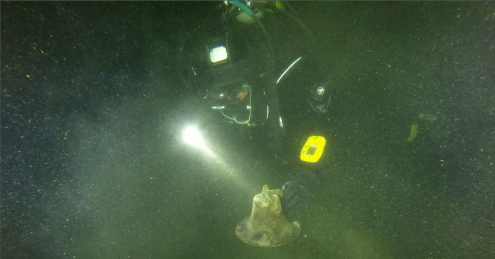 A diver shines a light on the bell of the shipwreck of the Little Harbor Launch