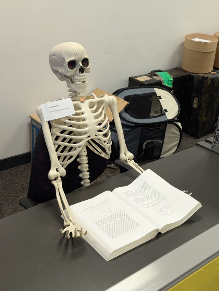 skeleton reading a book with glowing red eyes and a sign that says "do not disturb. Bob is still trying to graduate."