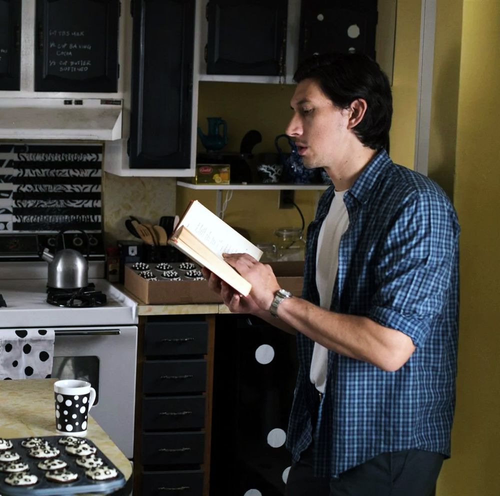 Adam Driver as Paterson, reading poetry in a black and white themed kitchen with a polka dot coffee cup on the counter in front of him