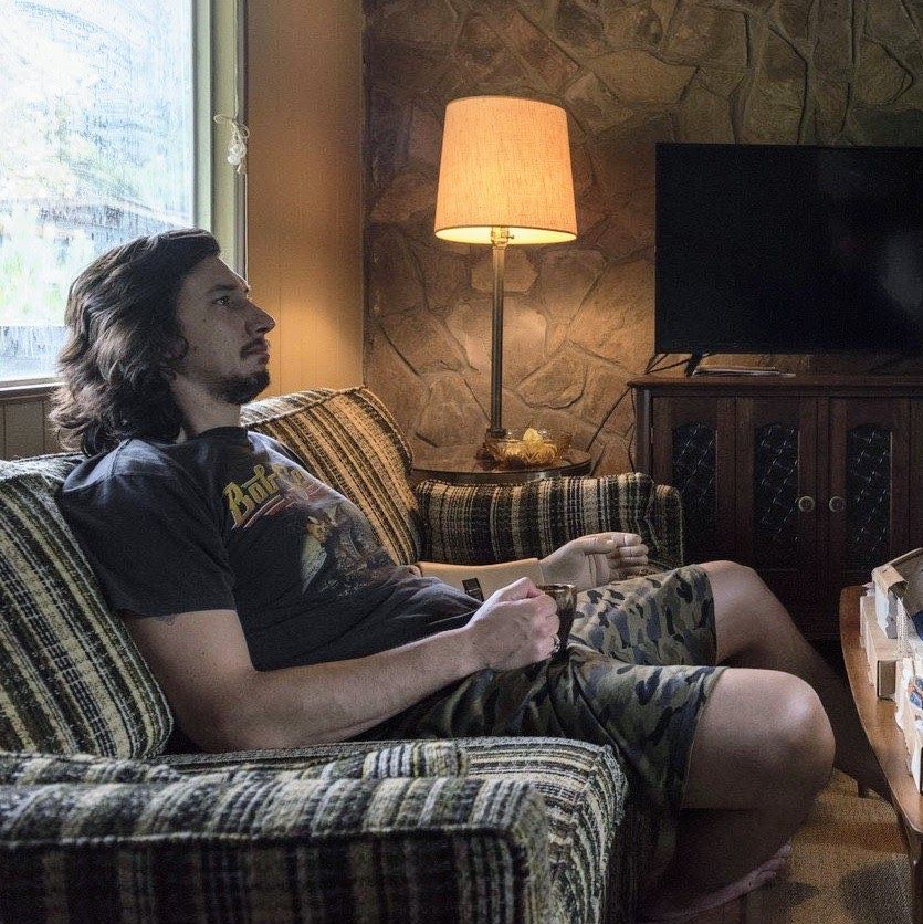 Adam Driver as Clyde Logan sitting on a sofa with a coffee mug in hand