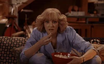 a woman is sitting on a couch eating popcorn while watching tv .