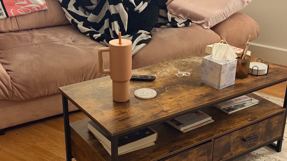 a pink tumbler on a wood coffee table. a pink couch in the background with a black and white blanket and pink pillow. 