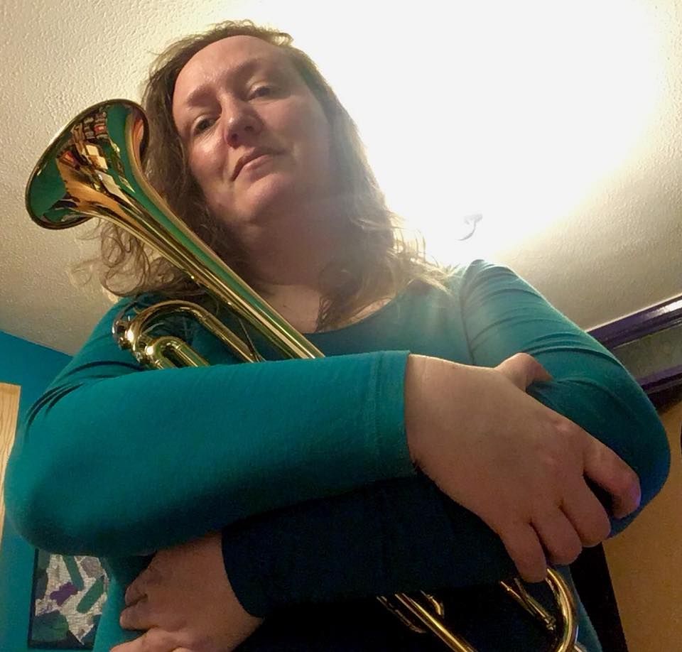 Blonde, white, chubby woman embracing a brass trumpet
