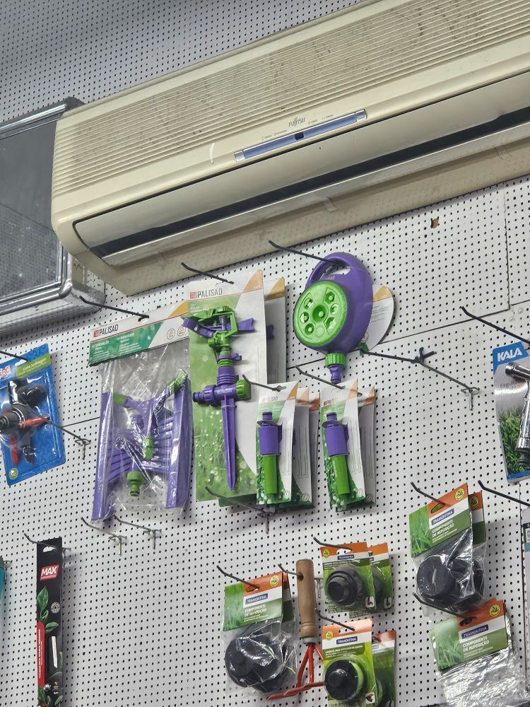 Parede de uma ferragem, nela se encontram diversos produtos para regar as plantas. Todos sao verde e roxo