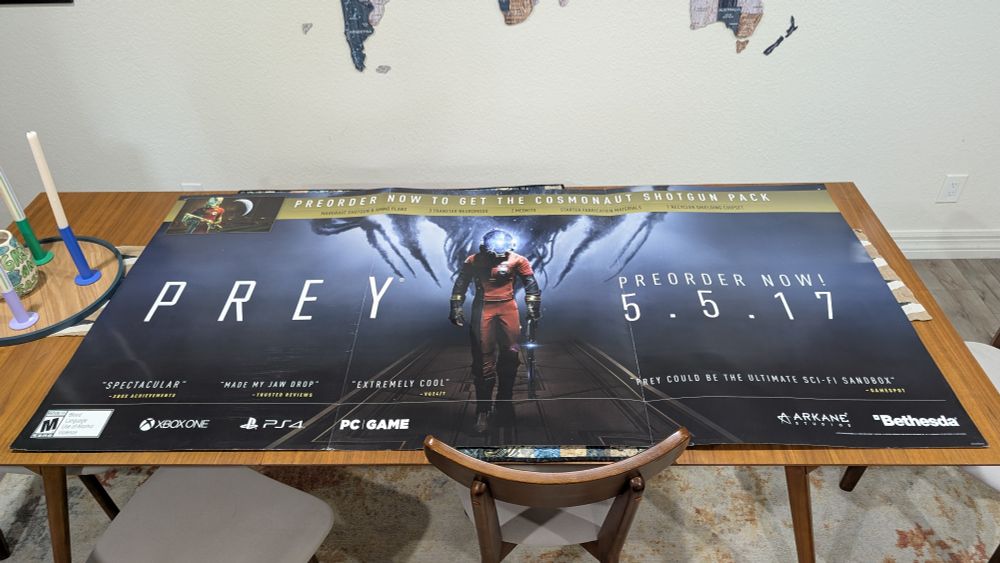 6 ft x 3 ft Prey (2015) preorder ad. 
It features a man (Morgan) in an orange space suit with the text "PREY preorder now 5.5.17"
There are testaments from various video games outlets. 
An M rating, logos for Xbox One, PS4, and PC, as well as Arkane and Bethesda. 