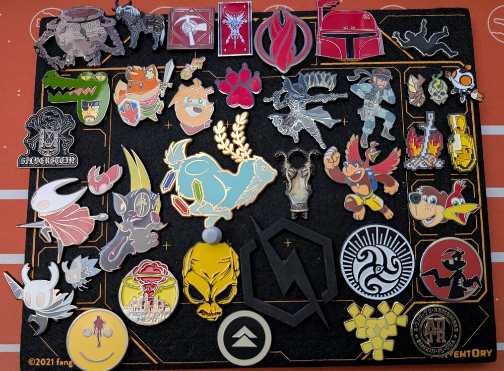 A black foam pin board covered in various pins. 
There are pins from Hollow Knight, Cuphead, Cyberpunk 2077, Banjo-Kazooie, Ty the Tasmanian Tiger, Bloodborne, Metal Gear Solid, Dark Souls, Elden Ring, Ghost of Tsushima, Pitfall, Star Wars, Pillars of Eternity, and more. 