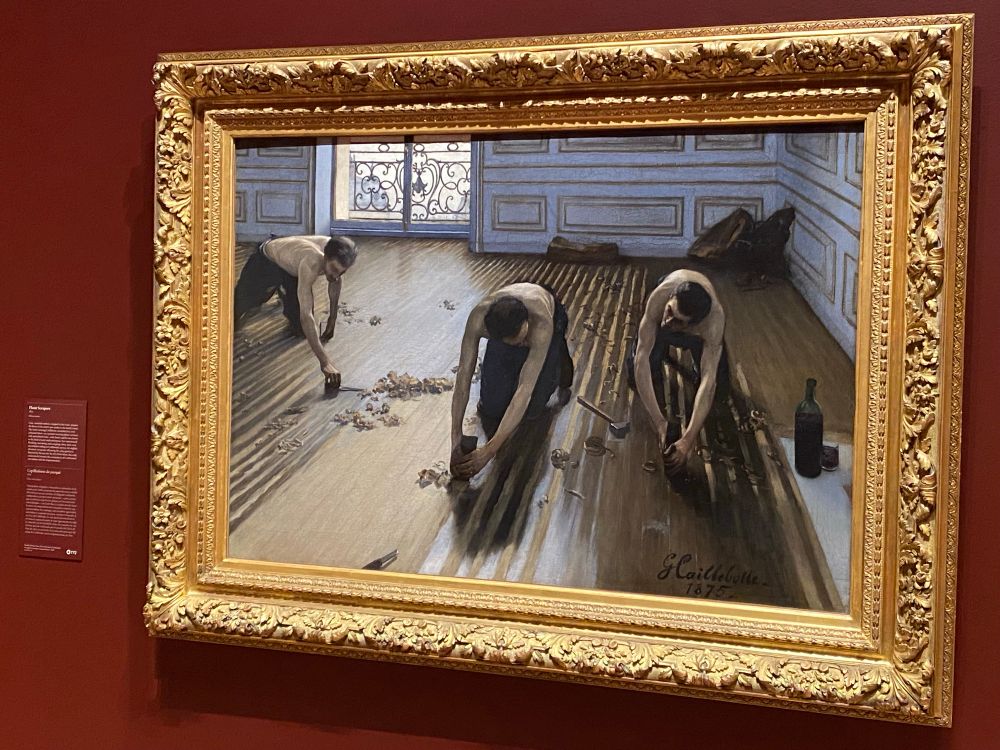 A picture of the painting Floor Scrapers by Gustave Caillebotte at the Getty Museum. In it, three shirtless men are using hang tools to strip/sand wood flooring. 