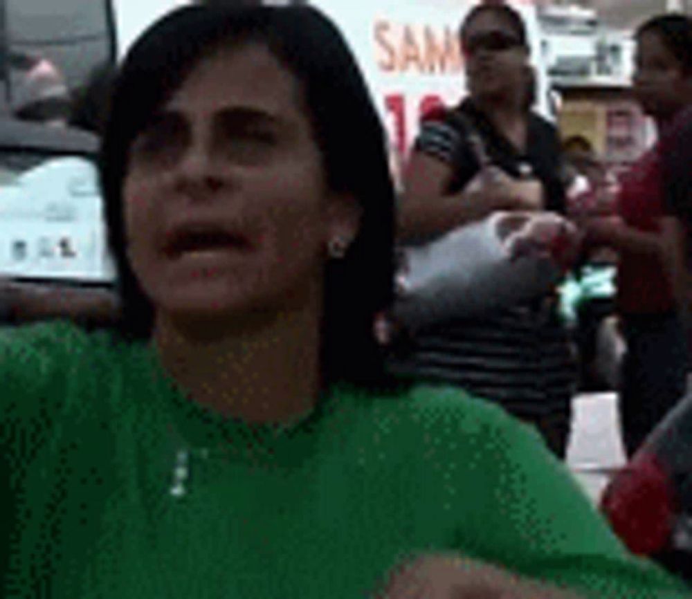 a woman in a green shirt is making a funny face while standing in front of a crowd of people .