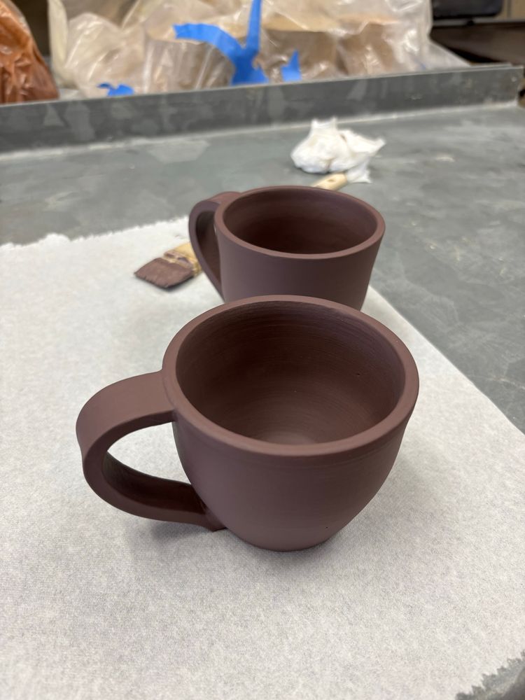 Two brown mugs with handles sit on a white surface.