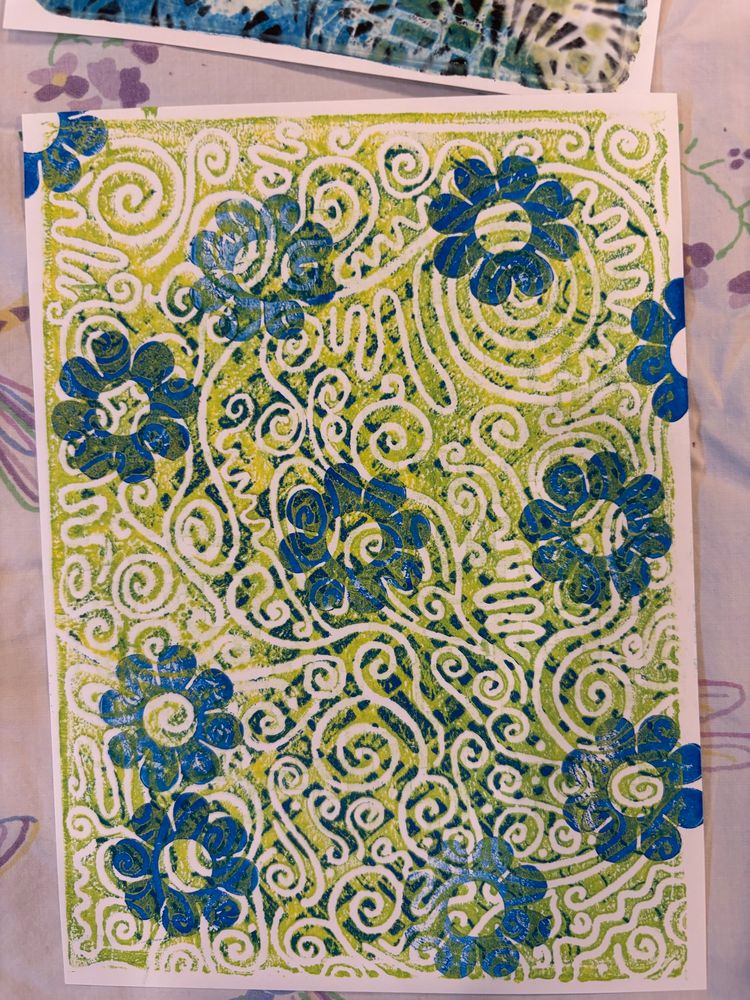 Gelli printed white rectangular paper with chartreuse squiggles in the background and blue flower shaped stamps in the foreground.
