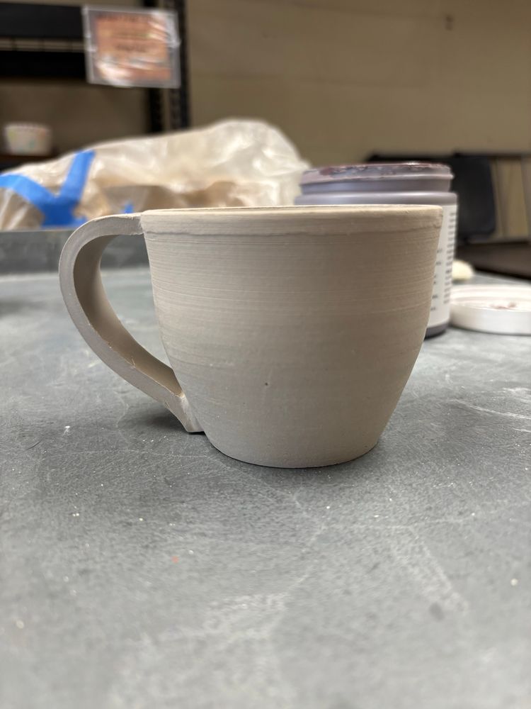 A small coffee mug with handles sit sits on a grey table.