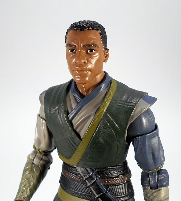 closeup of a marvel legends mordo figure from the dormammu build-a-figure wave. he has his green and tan kamar tag costume from the doctor strange movie, and a head with a terrible likeness of chiwetel ejiofor, seriously he almost looks more like young keith david it's way off, and it doesn't help that this was several movies before they rolled out the face printing tech which gave photorealistic paint deco on the 3d-scanned faces. anyways so he just kind of looks like a generic black guy with short cropped curly hair, but bonus, that means he looks like a comics accurate maxam minus the clear visor stye goggles. and he was common and didn't sell great so he's still cheap on the aftermarket.